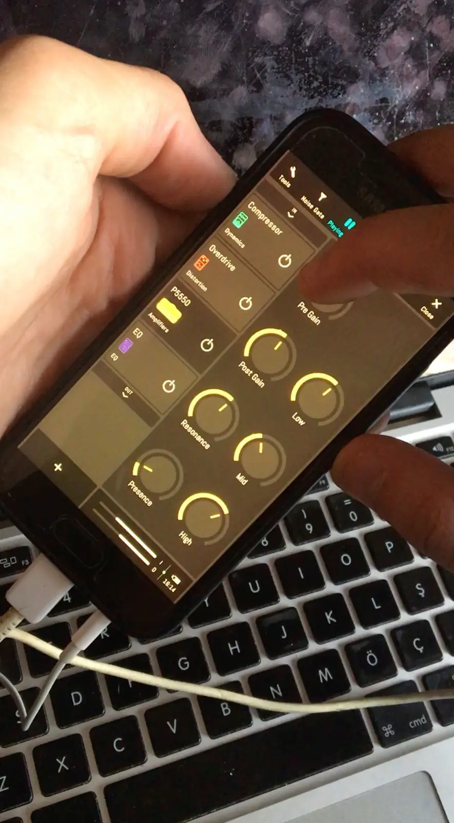 A phone in one hand over a laptop keyboard, open on the studio with the P5550 amp's yellow knobs, a finger of the other hand on one of them.