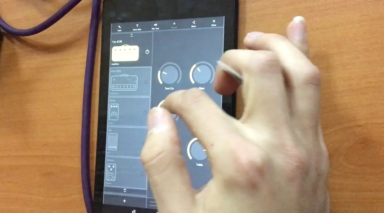 A tablet flat on a wooden table, open on the studio, a hand reaching across it to pinch one of the knobs.