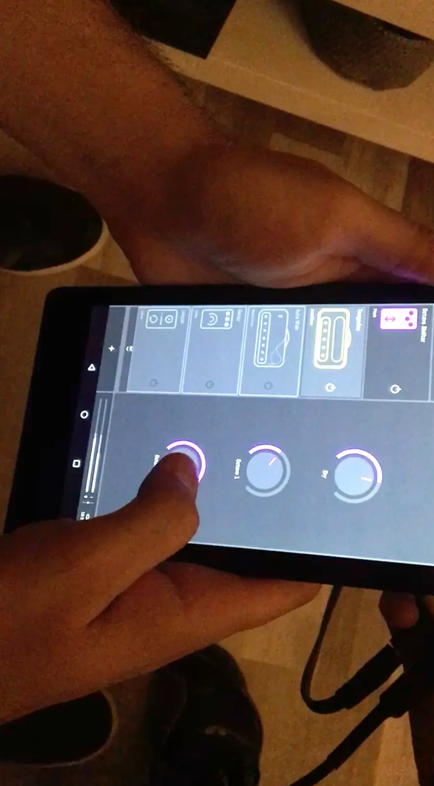 A tablet held sideways in two hands, a finger on one of the studio's purple knobs.