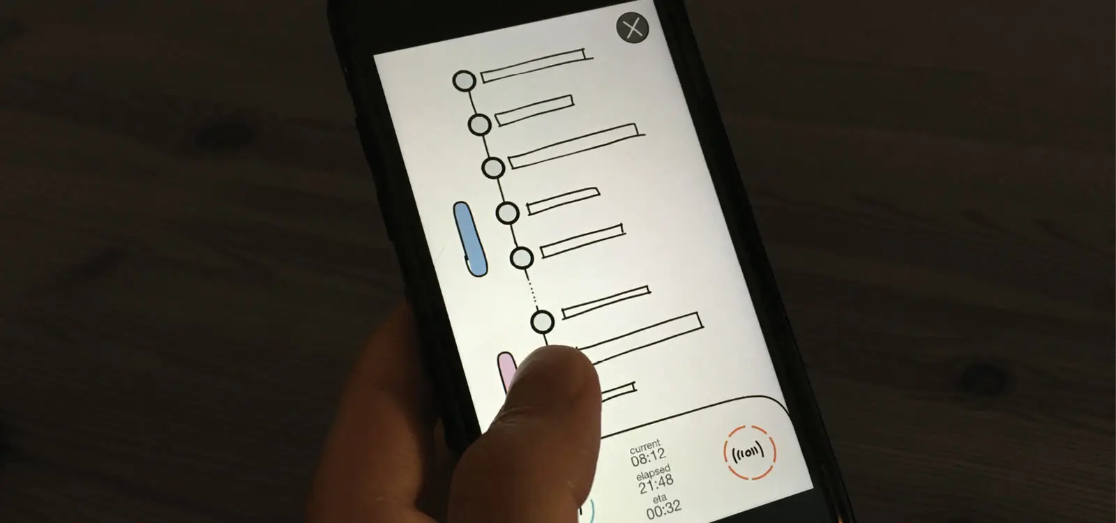 A hand holding a phone in a dim room. On screen, the sketched Track Mode, a line of stops with a close button, and the current, elapsed and arrival times in the corner.